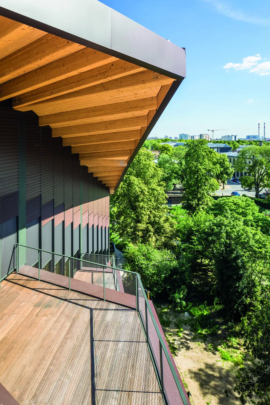 Terrasse en bois sous un d&eacute;bord de toiture &agrave; charpente apparente, face au parc