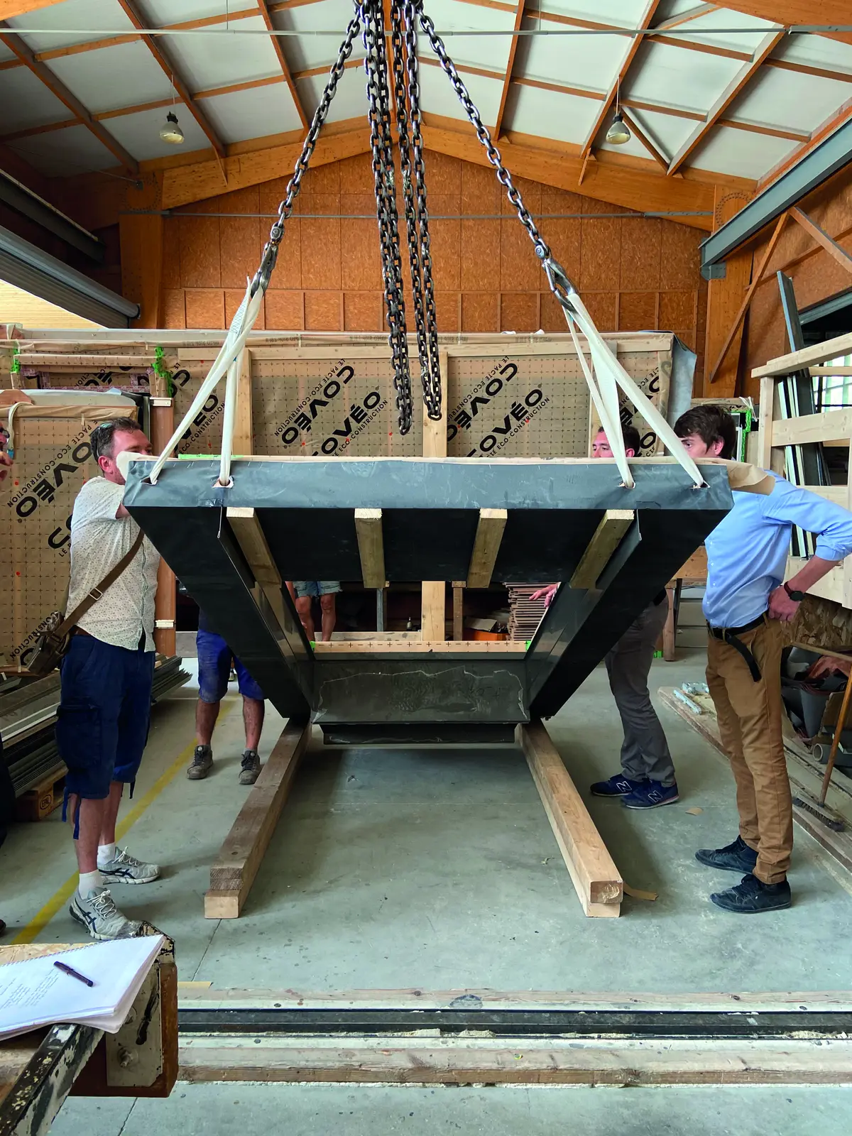 Module de plancher en bois suspendu &agrave; des cha&icirc;nes dans un atelier, observ&eacute; par des visiteurs