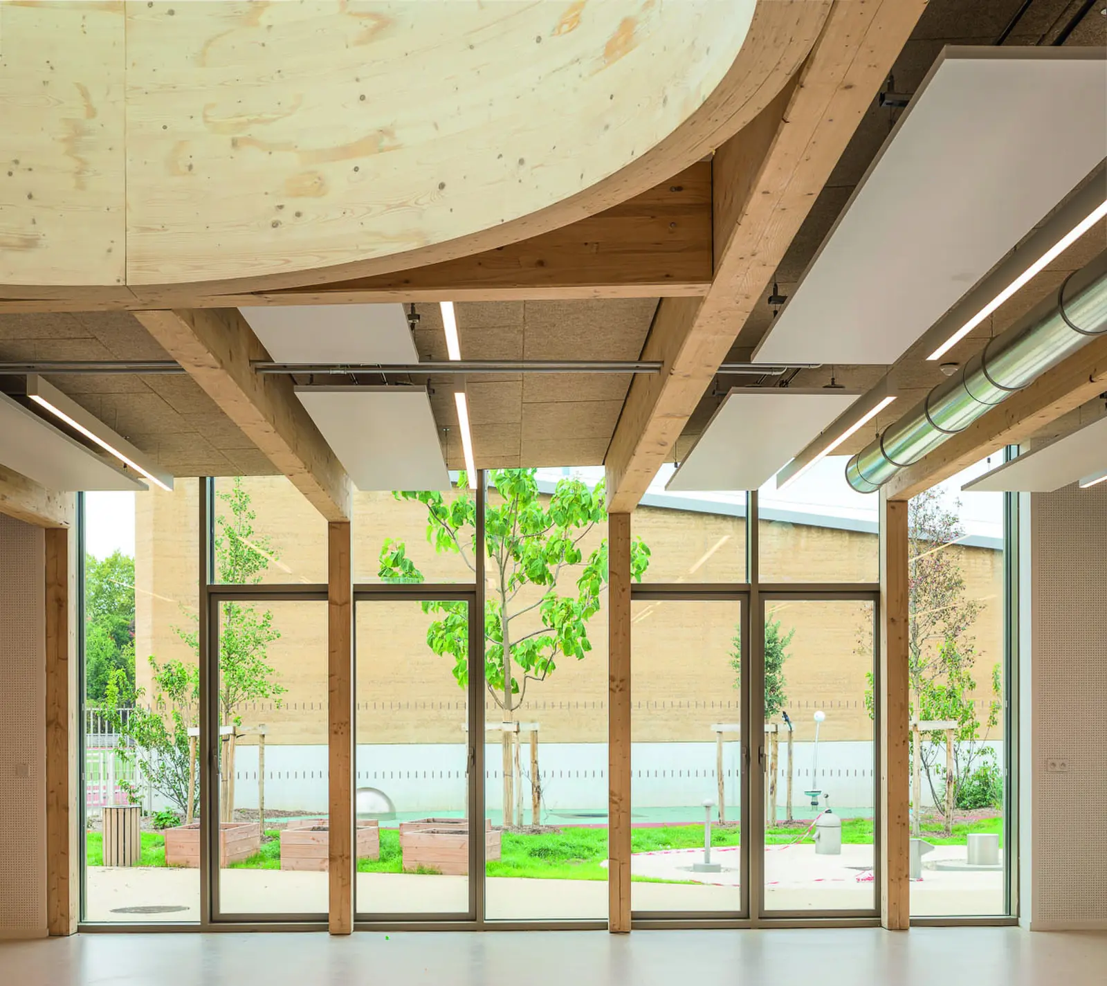 Espace int&eacute;rieur avec poutres en bois lamell&eacute;-coll&eacute; et grandes baies vitr&eacute;es
