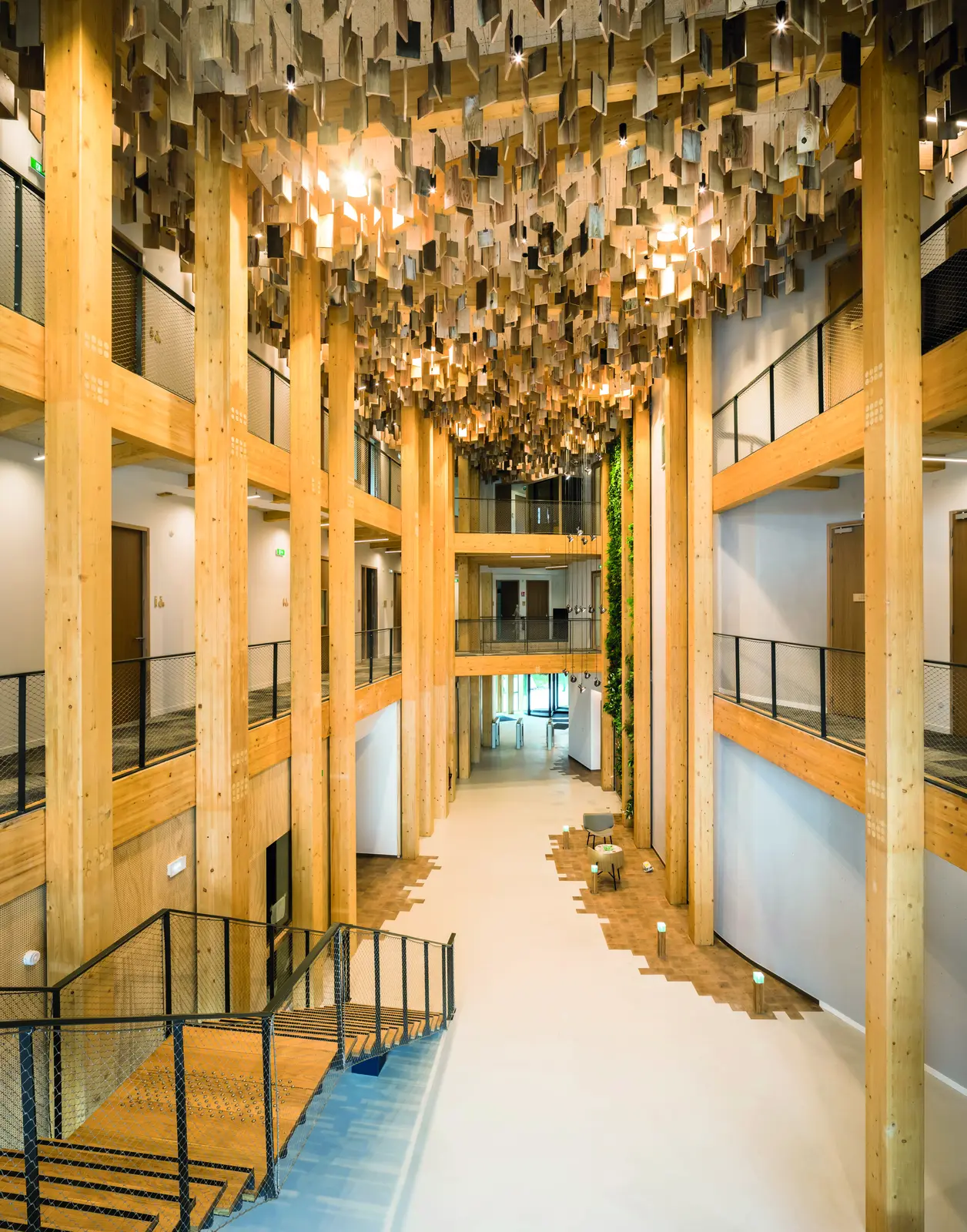 Rue int&eacute;rieure sur plusieurs niveaux bord&eacute;e de grands poteaux en bois, avec escalier et plafond en tavaillons suspendus