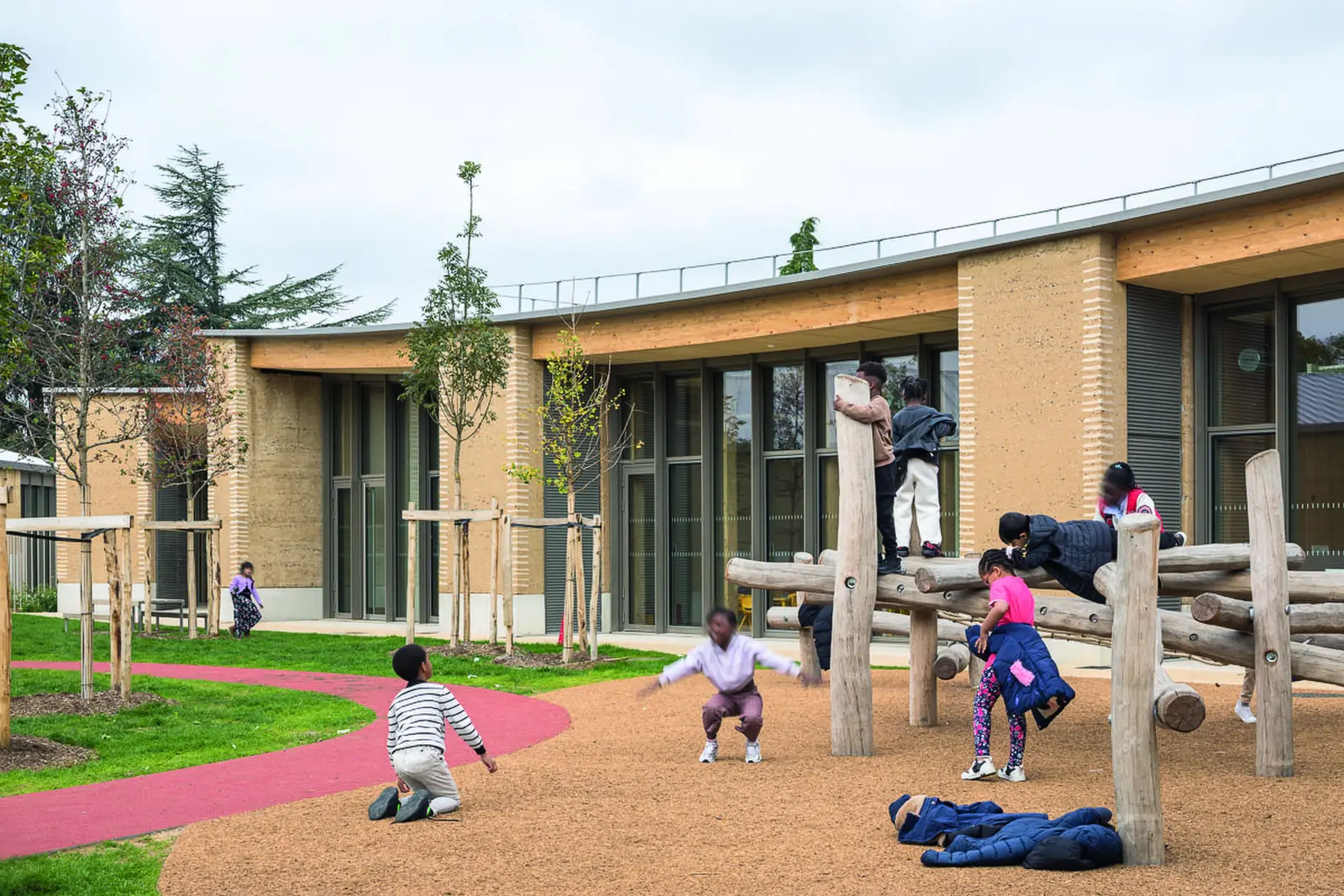 Enfants jouant sur une structure en rondins devant un b&acirc;timent en pis&eacute;