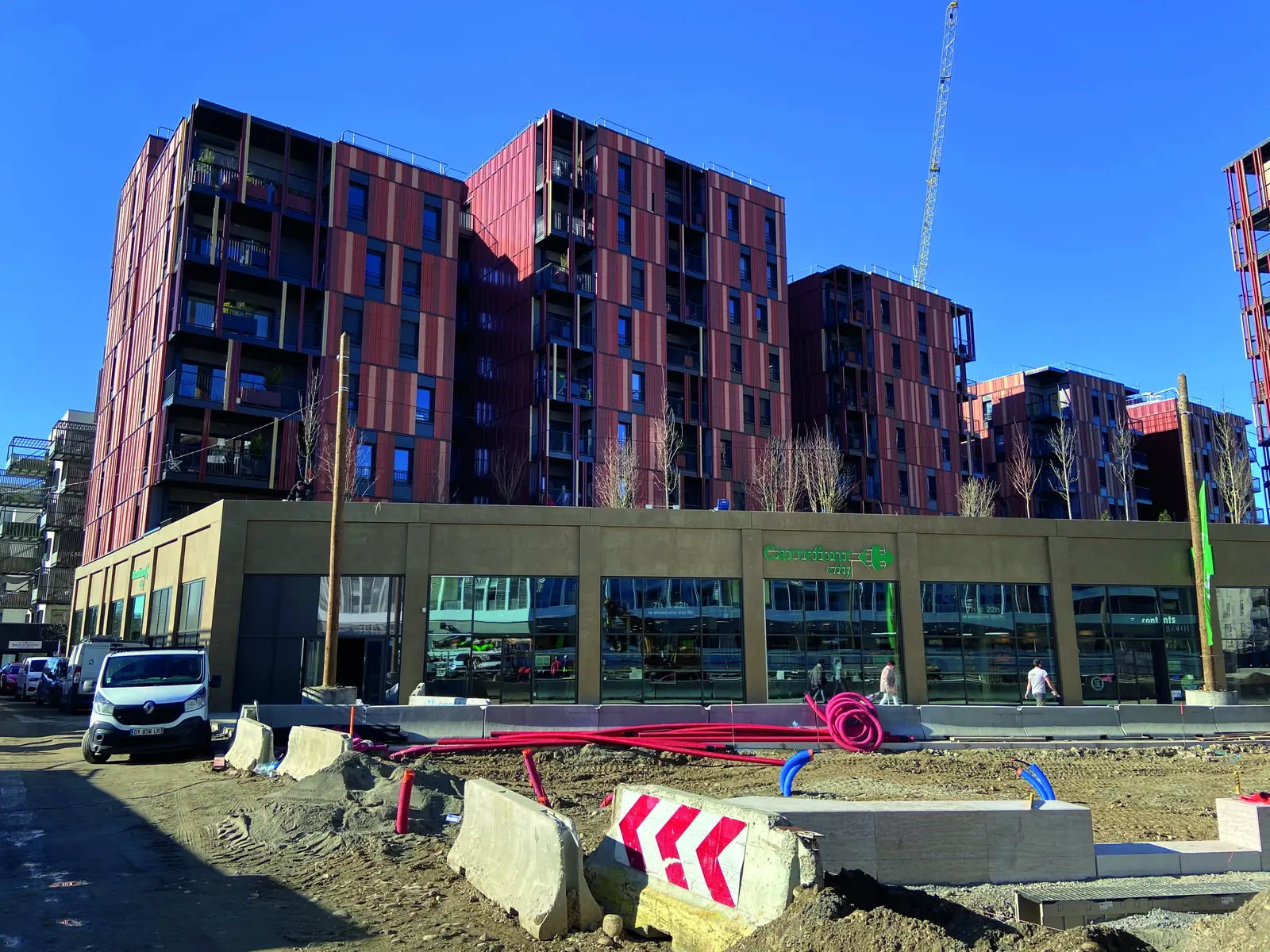 Immeubles d&rsquo;habitation &agrave; fa&ccedil;ades rouges du chantier Wood Art, rue en travaux au premier plan