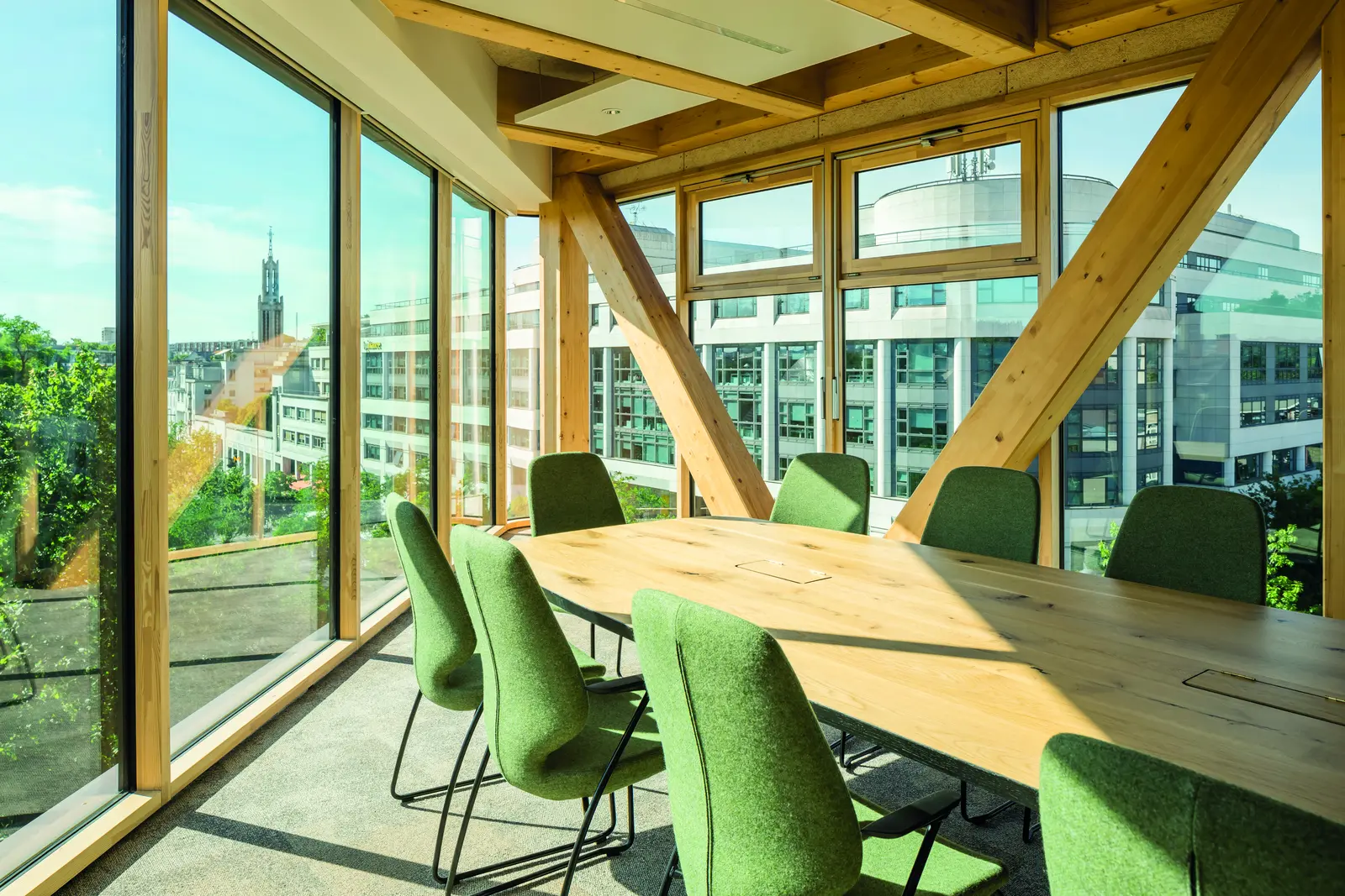 Salle de r&eacute;union vitr&eacute;e avec structure en bois en V et chaises vertes