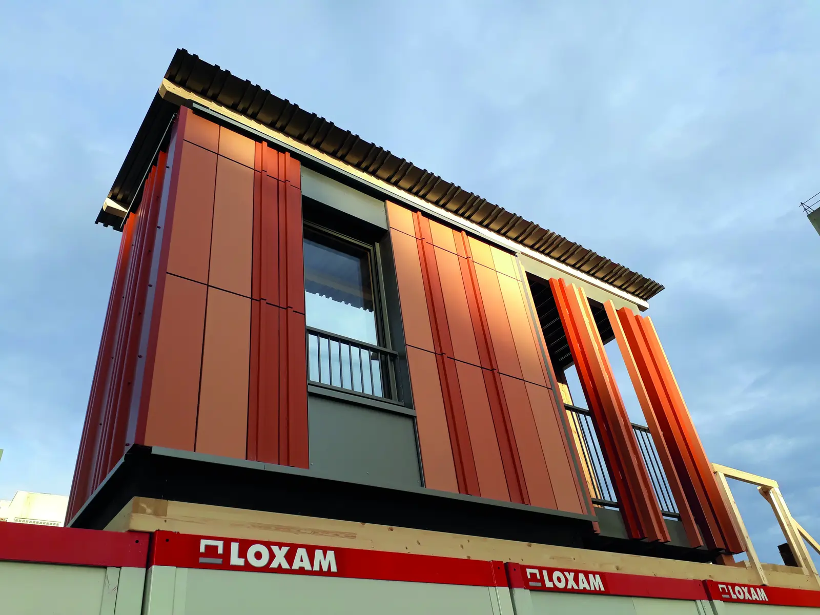 Module de b&acirc;timent &agrave; bardage orange en terre cuite pos&eacute; sur des conteneurs de chantier