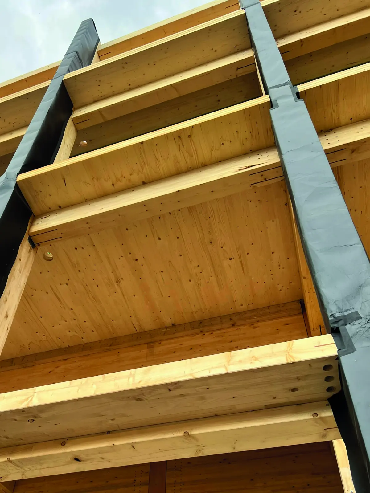 Vue en contre-plong&eacute;e de poutres en lamell&eacute;-coll&eacute; et d&rsquo;un plancher en CLT