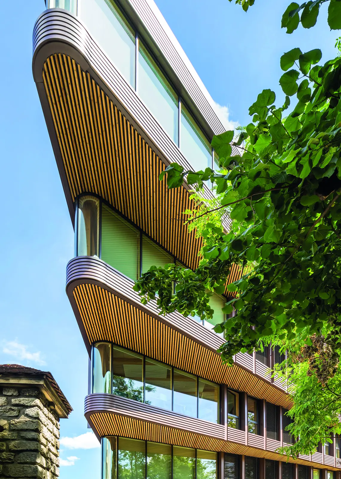 Fa&ccedil;ade aux balcons courbes habill&eacute;s de lames de bois au milieu des arbres