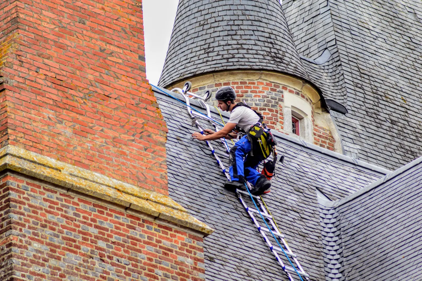 Couvreur montant à une échelle sur une toiture en ardoise