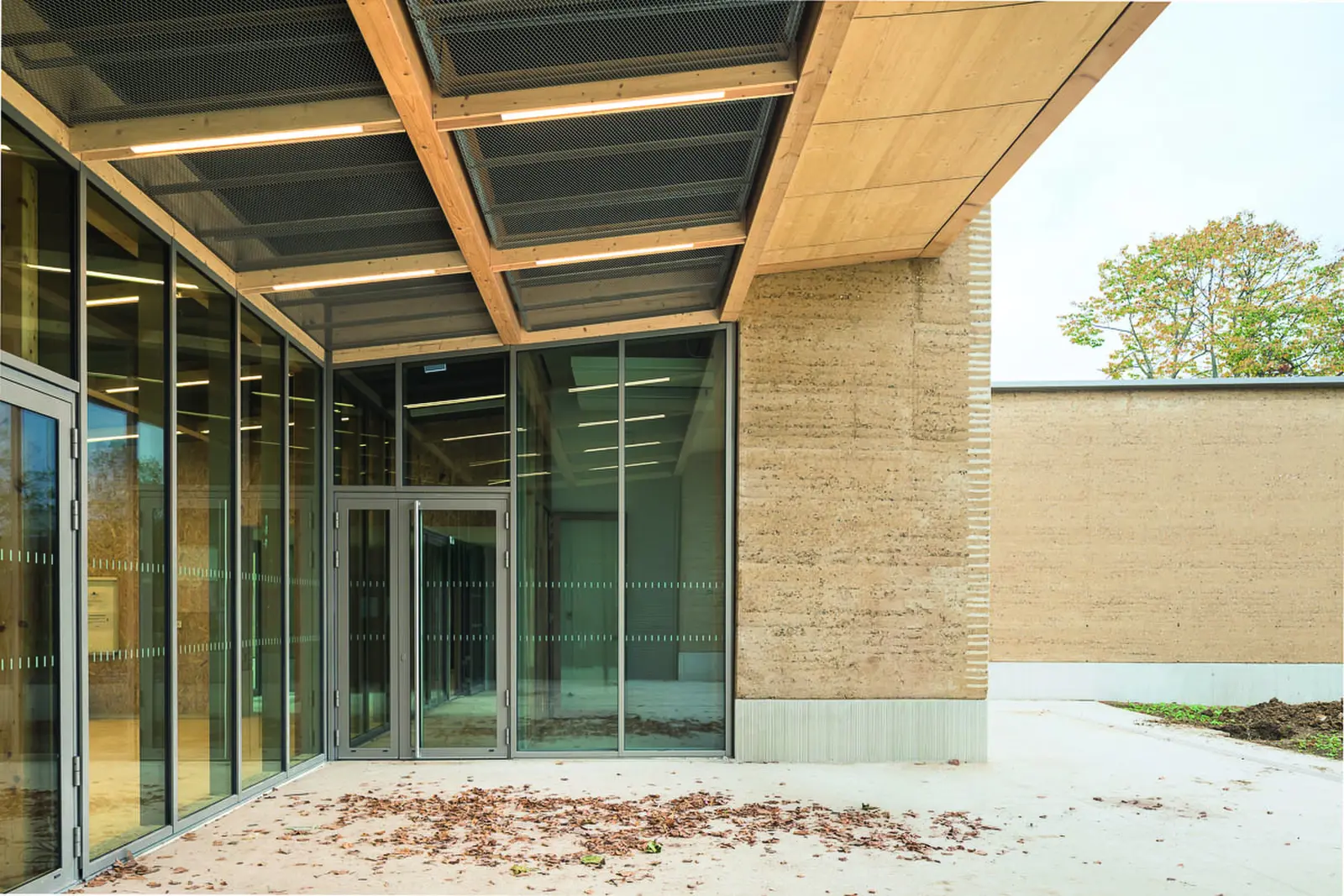 Passerelle vitr&eacute;e entre deux b&acirc;timents aux fa&ccedil;ades en pis&eacute;, sous une charpente bois